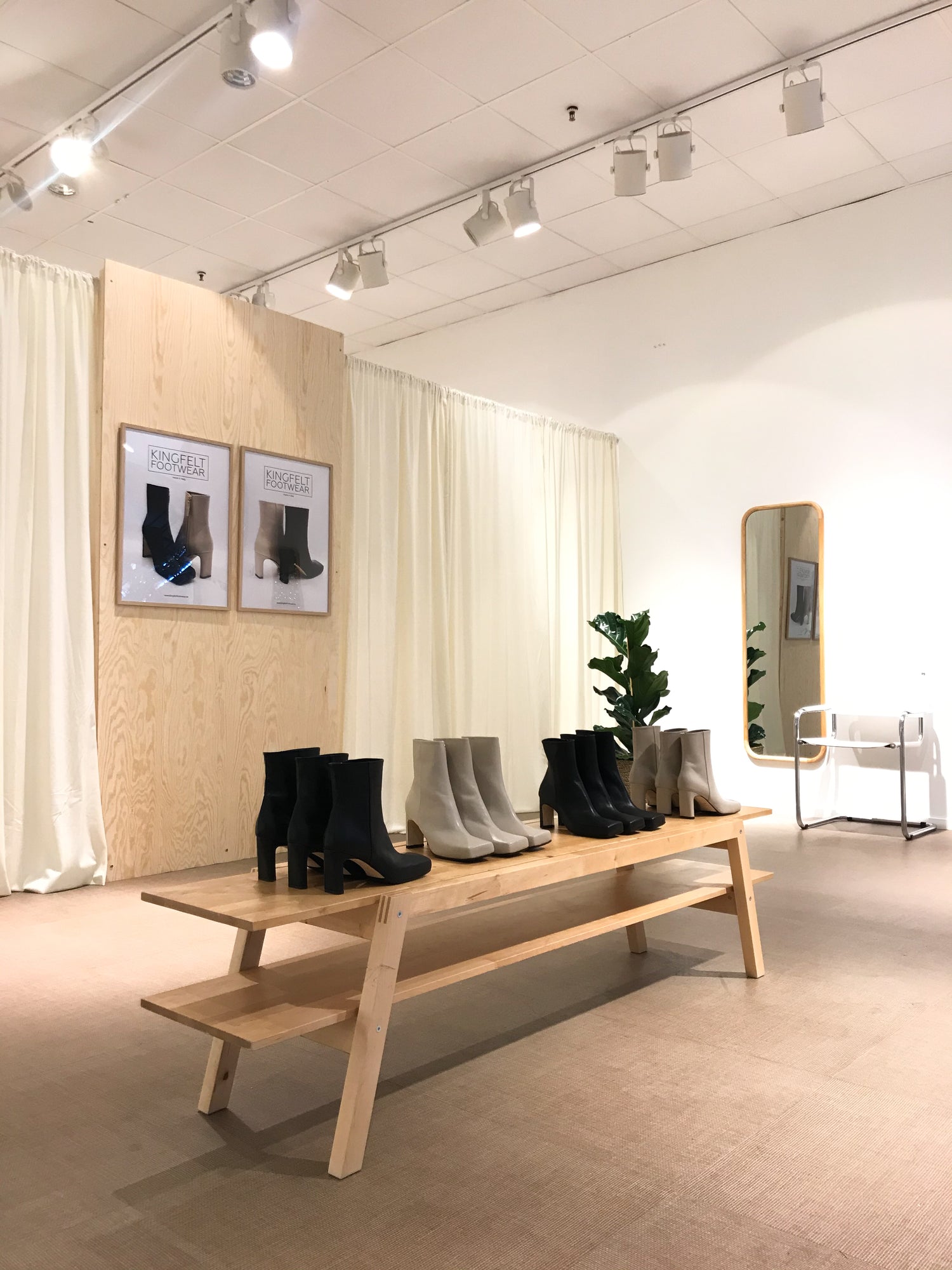 POP-up butik KINGFELT FOOTWEAR i Linden köpcentrum i Norrköping. Creme färgade sammets gardiner som täcker väggen tillsammans med plywoodskiva med tavlor på handgjorda skinnstövletter. En träbänk med svarta och beiga skinnstövletter på display.